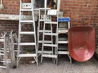 Front view of assorted ladders and wheelbarrow arranged against brick wall