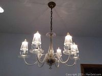 Six-armed clear hanging ceiling light fixture illuminated and suspended from the ceiling in a room with recessed lighting.
