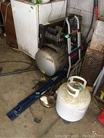 Air compressor, folding sawhorse, hand truck, and propane tank displayed in workshop area showing wear and dirt.
