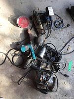 Top view of multiple power tools including sanders and router piled on ground