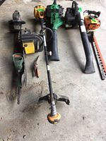 Full set of gas powered gardening tools including trimmers, chainsaw, leaf blower, pruners on concrete floor, showing all items in the lot.