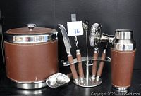 Full view of bar set components on shelf including ice bucket, cocktail shaker, bar tools on stand