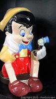 Front view of the ceramic cookie jar showing Pinocchio sitting with Jiminy Cricket in his hand.