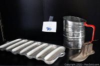 Three antique items on display: corn cob pan, sifter, and cast iron shoe plate.