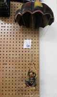 Full view of the clown hanging sculpture attached to a pegboard wall demonstrating the proportional size of parachute and seated clown figure below.