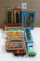 Overview of 11 piece HO scale railroad train lot showing boxed Tyco train cars, Life-Like landscaping materials, and track sections.