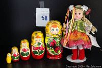 Full view of the Madame Alexander doll in Ukrainian traditional costume standing next to the 5-piece Russian nesting doll set, showing the size and color coordination.
