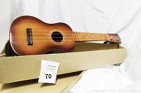 Vintage all wood ukulele resting inside original box, showing the body, strings, and neck with clear wood grain and sunburst finish.
