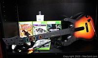 Photo of Guitar Hero guitar controller, four Xbox 360 game cases, one controller, and adapter cords on black shelf
