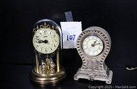 Both vintage table top clocks shown side by side on black surface for lot overview