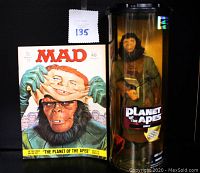 Photo showing the Mad Magazine cover with an ape holding a human face mask and the sealed Planet of the Apes Zira action figure in cylindrical packaging beside it
