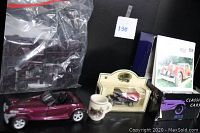 Photo showing the maroon Maisto Plymouth Prowler model car, sealed parts for the 1955 Chevy Stepside kit in a clear plastic bag, the gas truck in packaging, Daimler shot mug, and boxed set of giant classic car cards.