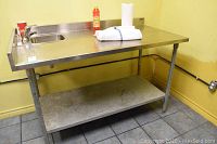 Full view of stainless steel prep table with sink and lower shelf against yellow wall