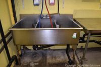 Full-frontal view of stainless steel three-bay sink showing mounting legs and plumbing connections