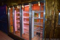 Front view of four glass doors with interior wire shelving and overhead lights in wooden frame.