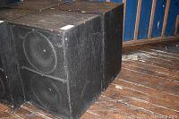 Front and side view of two black wood speaker cabinets on wooden floor