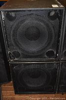 Front view of two black speaker enclosures stacked, showing mesh grills and 18" woofers.