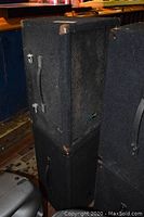 Two black speaker cabinets stacked, showing overall appearance and carpeted finish