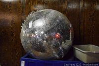 Disco ball on blue crate against wood panel wall, chain draped over top, showing full mirrored sphere.