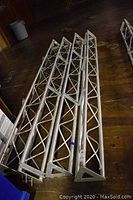 Four aluminum truss towers laid side by side on wood floor