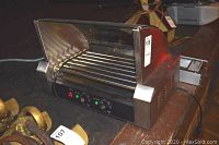 Side view of stainless steel hot dog roller showing rollers, housing and control panel