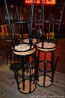 Group of six stools stacked upside down on top of remaining stools showing black frames and wooden seats