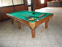Angled view of table showing green felt, leather pockets, wooden frame, turned legs, and pool accessories on surface