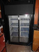 Front view of commercial refrigerator showing black cabinet, two sliding glass doors and multiple interior wire shelves with blue liners.
