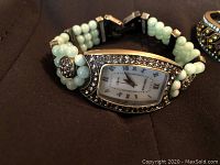 Close-up of rectangular-faced watch with triple strand light green bead band and rhinestone decorations.