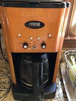 Orange Cuisinart coffee maker with black accents and digital display showing time 11:12, control knobs for settings.
