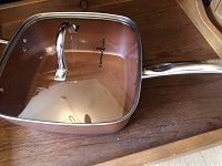 Square copper-colored cookware pan with glass lid and metal handle, pan's handle extended to side, Copper Chef branding on lid and pan interior visible.
