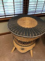 Round wicker table showing natural and dark wicker weaving on the tabletop and lattice wicker design on the base with three stout legs.