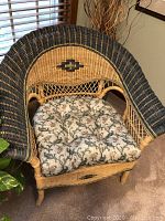 Front and side angled photo of the wicker chair showing the curved backrest, woven black and natural wicker, and floral cushion seat.