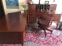 Photo of L-shape cherry finish wooden desk and swivel chair on patterned rug