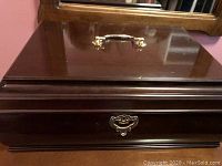 Closed view of the large cherry finish wooden jewelry box with gold-tone handle and lock plate.