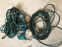 Lot of two long green electric cords and a green outdoor floodlight with stake.