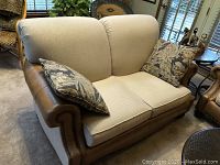 Front view of loveseat showing two seat cushions, back cushions, rolled leather arms and two floral pillows