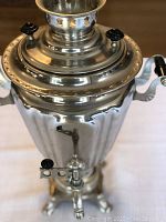 Side view of the vintage electric Russian samovar showing its fluted body, black heat-resistant handle, and spigot.