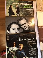 Top view of three Simon and Garfunkel vinyl album covers stacked, showing the album 'Sounds of Silence' and two others partially visible.