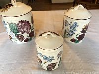 Three ceramic canisters with floral designs placed on a table with a beige tablecloth.