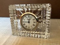 Front view of Waterford crystal clock showing white clock face with black Roman numerals and gold-tone bezel with clear cut crystal body.