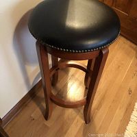 Full view of swivel barstool showing round black padded seat with nailhead trim and wooden base with footrest ring.