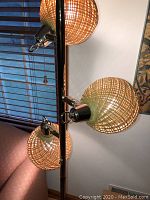 Close-up photo showing two of the spherical woven rattan lampshades mounted on dark metal poles with brass fitting accents.