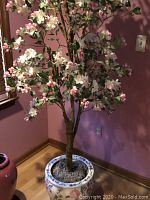 Full faux cherry blossom tree with pink and white blooms and green leaves against pink wall