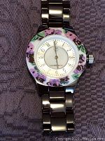 Close-up of front dial showing floral pattern and time markers on watch face.