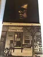 Front cover of Elton John's 'Tumbleweed Connection' vinyl album featuring a rustic storefront with various vintage signs.