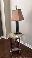 Side view of handmade octagonal side table with mother of pearl inlay topped with a table lamp, showing wood flooring and wall corner.
