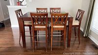 Full view of bar height dining table surrounded by six matching chairs