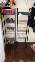 Two black metal shelving units on wheels, each with three wire shelves and solid top shelf, placed side by side showing wear and some shoes stored on one unit.