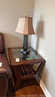 Wood and glass side table featuring dark wood frame, glass top, and slatted bottom shelf next to a brown leather sofa